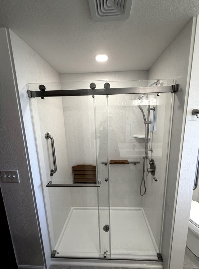Walk-in shower with sliding glass door and teak bench